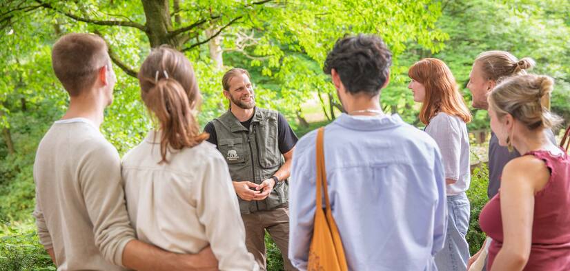 Gruppe mit Pfleger Eine Gruppe Menschen steht vor einem Mann mit Zoo-Weste und hören gebannt zu