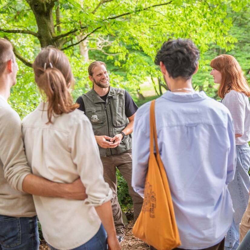 Gruppe mit Pfleger Eine Gruppe Menschen steht vor einem Mann mit Zoo-Weste und hören gebannt zu