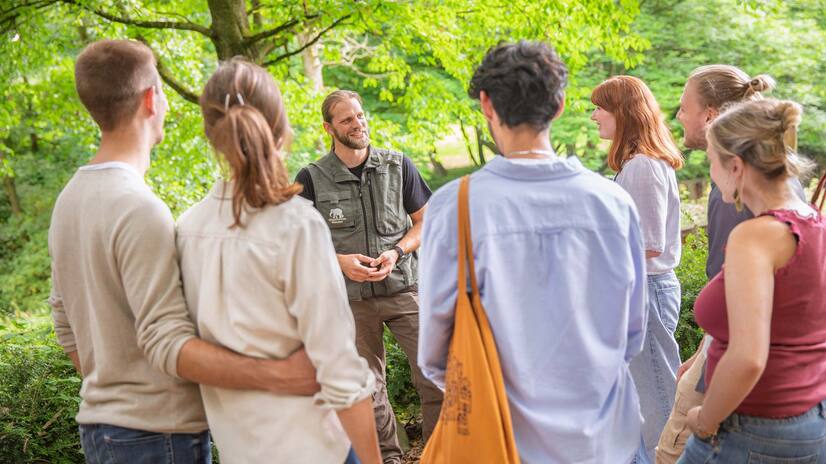 Gruppe mit Pfleger Eine Gruppe Menschen steht vor einem Mann mit Zoo-Weste und hören gebannt zu