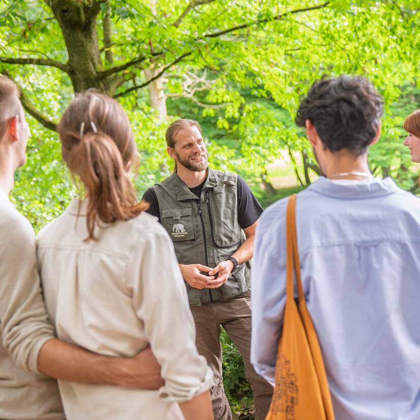 Gruppe mit Pfleger Eine Gruppe Menschen steht vor einem Mann mit Zoo-Weste und hören gebannt zu